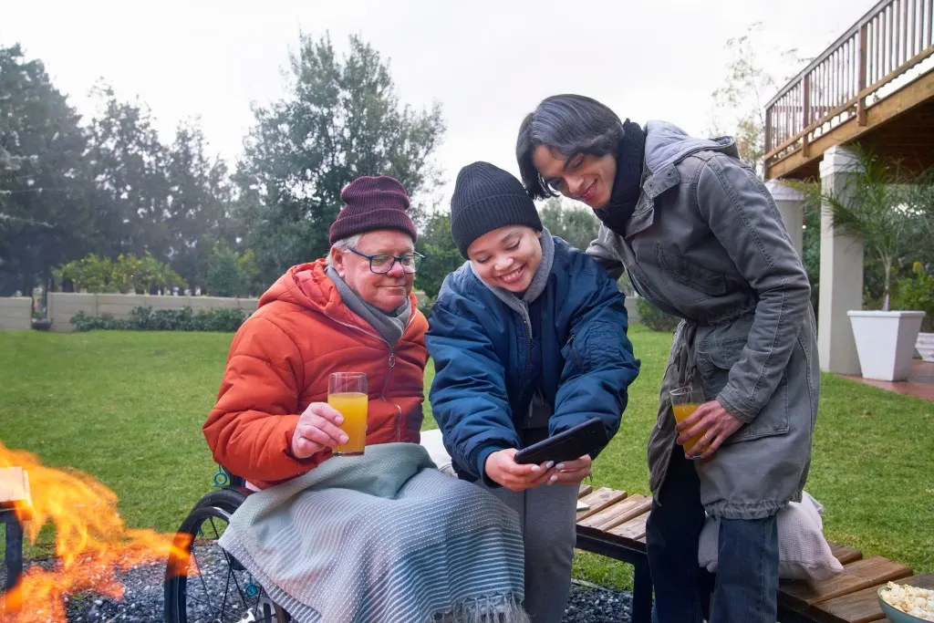 Disabled man in wheelchair looking at phone with carers