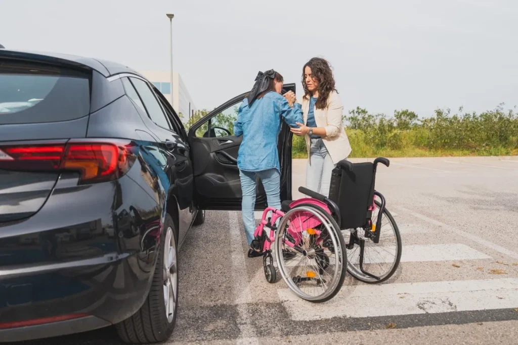 Carer helping disabled woman out of wheelchair and into a car